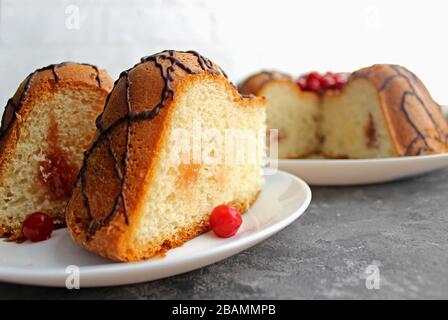 Kuchenscheiben auf einem Teller. Im Hintergrund steht der Kuchen selbst. Auf dunklem und hellem Hintergrund. Erdbeere und Creme mit Zucker füllen Stockfoto