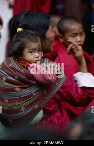 Eine bhutanische Mutter trägt ihr Kind während des jährlichen Thimphy Tsechu Festivals in einer Schlinge auf dem Rücken. (12-10-89) BX61 Stockfoto