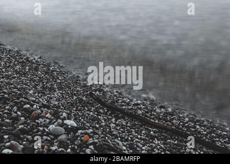 Ein Baum am Strand, auf Kieselsteinen und am Meer. Ein langer Belichtungsschuss Stockfoto