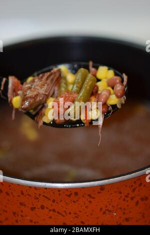 Großer Löffel, der herzhaftes hausgemachtes Rindfleisch und Gemüsesuppe aus einem Topf zubereitet. Nahaufnahme. Bunt. Stockfoto