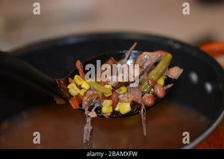 Großer Löffel, der herzhaftes hausgemachtes Rindfleisch und Gemüsesuppe aus einem Topf zubereitet. Nahaufnahme. Bunt. Stockfoto