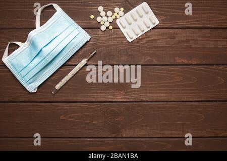 Medizinische Schutzmaske mit Medikamenten, Thermometer auf Holzhintergrund, Kopierraum Stockfoto