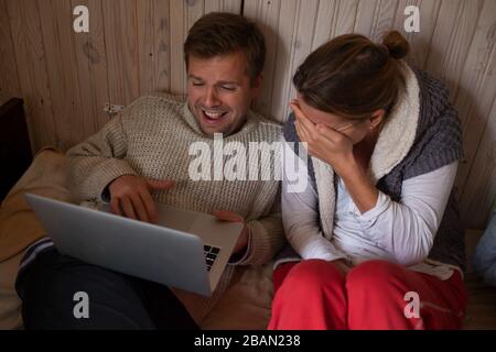 Lachende ältere Paare, die mit einem Laptop auf einem Bett in einem Schlafzimmer liegen Stockfoto