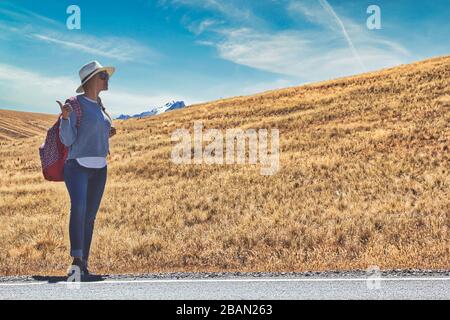 Schöne Frau hitchwandering auf der Straße im Wald, hitchwandering mit Daumen nach oben in einer Landstraße, Reise- und Hexerei Konzept. Stockfoto