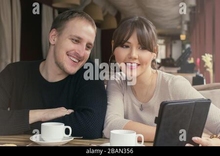 Eine asiatische junge Frau und ein kaukasisches Ehepaar im Café, die auf einen Tablet-Bildschirm blicken Stockfoto