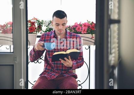 Gebärdeter Mann, der Bücher liest und Kaffee oder Tee trinkt Stockfoto