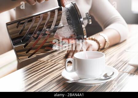 Das Mädchen gießt Tee in einer Tasse aus der französischen Presseleuchte Stockfoto