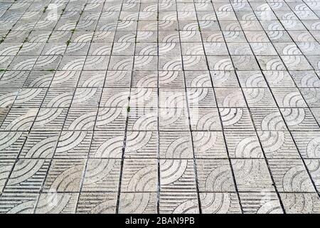 Textur aus grauen, quadratischen Betonpflastersteinen mit einem stilisierten Wellenornament. Pflastersteine mit diagonalem Muster. Hintergrund. Stockfoto