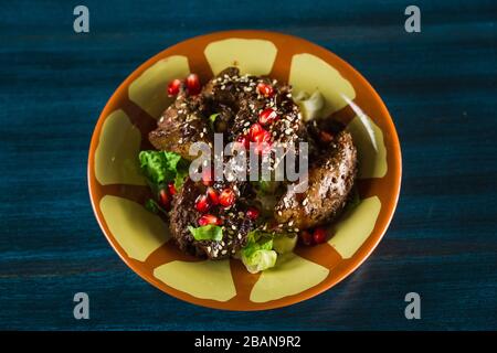 Pfanne mit traditionellem japanischem Yakitori-Gericht - gebratene Schachtelherzen mit Sesam, Teriyaki-Sauce und frischem Gemüse auf Holzbrett isoliert bei Stockfoto