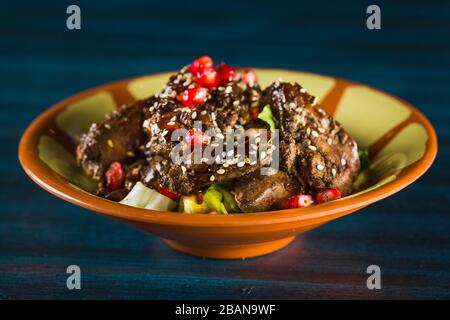 Pfanne mit traditionellem japanischem Yakitori-Gericht - gebratene Schachtelherzen mit Sesam, Teriyaki-Sauce und frischem Gemüse auf Holzbrett isoliert bei Stockfoto