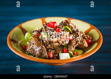 Pfanne mit traditionellem japanischem Yakitori-Gericht - gebratene Schachtelherzen mit Sesam, Teriyaki-Sauce und frischem Gemüse auf Holzbrett isoliert bei Stockfoto