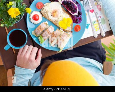 Wunderschönes, farbenfrohes Frühlingsfrühstück mit verschiedenen Speisen auf einem Holztisch mit Blumen und Händen, Blick von oben. Stockfoto