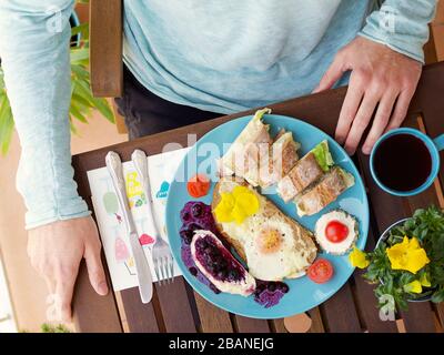 Wunderschönes, farbenfrohes Frühlingsfrühstück mit verschiedenen Speisen auf einem Holztisch mit Blumen und Händen, Blick von oben. Stockfoto