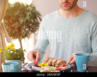 Wunderschönes, farbenfrohes Frühlingsfrühstück mit verschiedenen Speisen auf einem Holztisch mit Blumen an einem sonnigen Tag und einem Mann im Hintergrund. Stockfoto