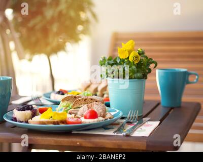 Wunderschönes farbenfrohes Frühlingsfrühstück mit einer Vielzahl an Speisen auf einem Holztisch mit Blumen an einem sonnigen Tag. Stockfoto