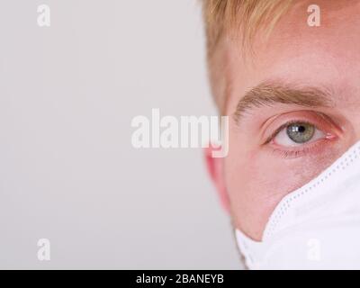 Nahaufnahme eines kaukasischen Manngesichts mit gelber Gesichtsschutzmaske mit grünen Augen und blonden Haaren, seit dem Ausbruch des neuen Coronavirus. Stockfoto