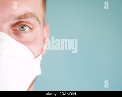 Nahaufnahme eines kaukasischen Manngesichts mit gelber Gesichtsschutzmaske mit grünen Augen und blonden Haaren, seit dem Ausbruch des neuen Coronavirus. Stockfoto