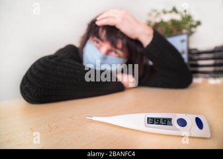 Coronavirus-Krankheit. Kranke Frau mit Gesichtsmaske. Hohe Temperatur am medizinischen Thermometer. Covid-19-Ausbruch. Fieber, Kopf- und Rachenschmerzen in Quarantäne. Stockfoto