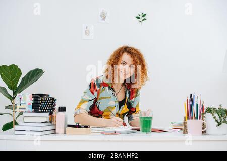 Frau zieht Aquarell, sie sitzt in farbiger Kleidung am Tisch Stockfoto