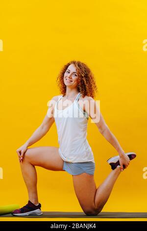 Fröhliche rothaarige lockige Frau, die ein Stretchtraining macht Stockfoto