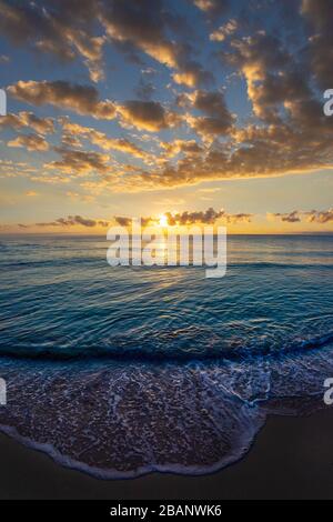 Wunderschöne Sonnenaufgangswolkenlandschaft über dem Meer mit Wellen, die auf den sandigen Strand rollen. Stockfoto