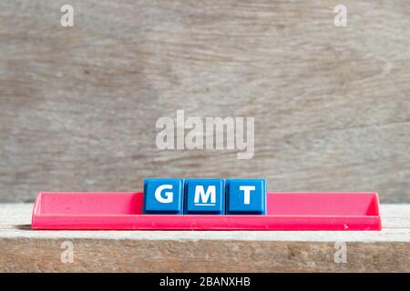 Fliesenbuchstabe auf rotem Rack in Wort GMT (Abkürzung von Greenwich Mean Time) auf Holzhintergrund Stockfoto