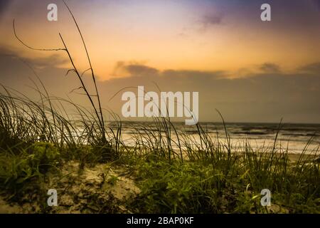 Nahaufnahme einer Sanddüne mit Wasser und Wolken im Hintergrund bei Sonnenaufgang Stockfoto