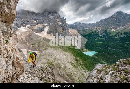 Junger Mann, Bergsteiger auf einer festen Seilstrecke, über Ferrata Vandelli, Blick auf Lago di Sorapis, Sorapiss-Rundkurs, Berge mit niedrigen Wolken, in die Dolden Stockfoto