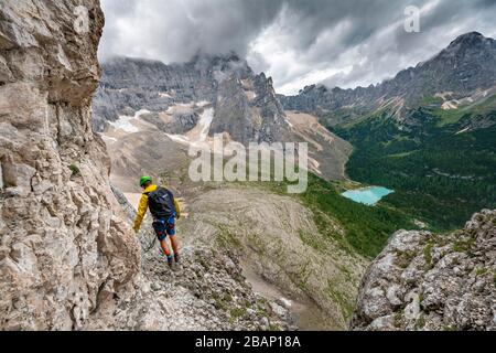 Junger Mann, Bergsteiger auf einer festen Seilstrecke, über Ferrata Vandelli, Blick auf Lago di Sorapis, Sorapiss-Rundkurs, Berge mit niedrigen Wolken, in die Dolden Stockfoto