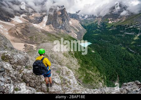 Junger Mann, Bergsteiger auf einer festen Seilstrecke, über Ferrata Vandelli, Blick auf Lago di Sorapis, Sorapiss-Rundkurs, Berge mit niedrigen Wolken, in die Dolden Stockfoto