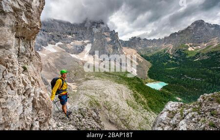 Junger Mann, Bergsteiger auf einer festen Seilstrecke, über Ferrata Vandelli, Blick auf Lago di Sorapis, Sorapiss-Rundkurs, Berge mit niedrigen Wolken, in die Dolden Stockfoto