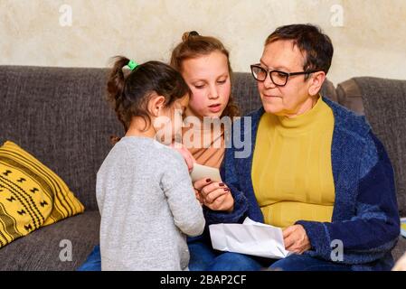 Oma, Die Alte Fotos Mit Enkeln Betrachtet, Um Die Erinnerung Zu Aktualisieren. Glückliche Familie, Gemütliche Heimmomente. Stockfoto