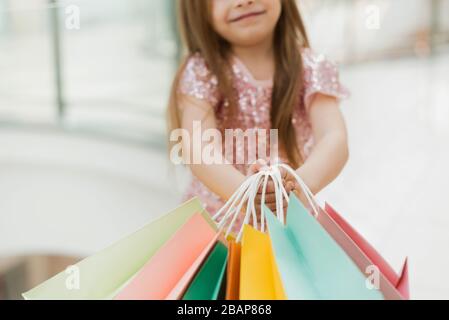 Ein kleines Mädchen hält mehrfarbige Pastelltaschen in den Händen. Das Konzept des Einkaufs, des Einkaufs im Einkaufszentrum. Nahaufnahme. Stockfoto