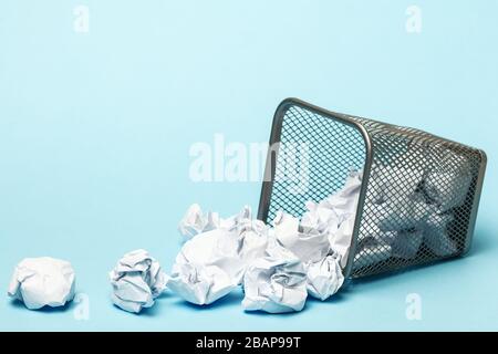 Umgekippter Papierkorb mit zerknitterten Papierkugeln auf blauem Hintergrund. Speicherplatz für die Kopie im Großraum. Stockfoto