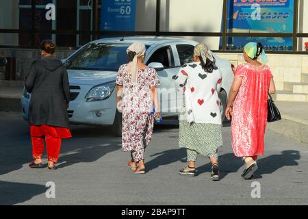 Blick von hinten auf eine Gruppe von vier usbekischen einheimischen Frauen, die bunte traditionelle Kleidung tragen. Der Alltag in Buchara, Usbekistan in Zentralasien. Stockfoto