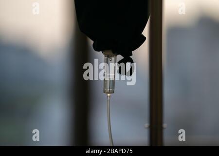 In der Nähe des medizinischen Werkzeugs tropft Kochsalzlösung im dunklen Silhouettenmotiv am Abendfenster. Stockfoto