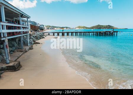 Ein kleiner Steg ragt über das blaue Wasser und den goldenen Sand von Grand Case Beach, Saint Martin (französische Seite) Stockfoto