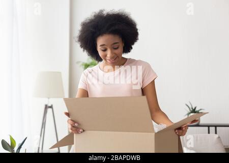 Afroamerikanische Frau öffnet Box und sieht mit einem Lächeln darin Stockfoto