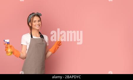 Lächelnde Frau in der Schürze, die Sprayer hält und auf den Kopierbereich zeigt Stockfoto