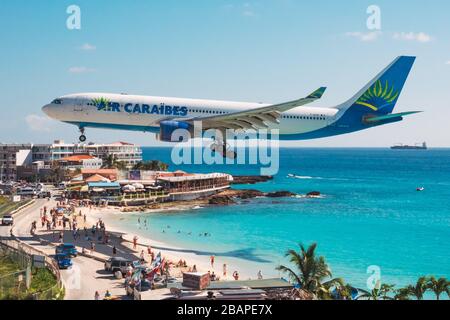 Ein Airbus A330-200 der Air Caraibes-Serie wirft einen Schatten auf Touristen am Maho Beach in St. Maarten Stockfoto