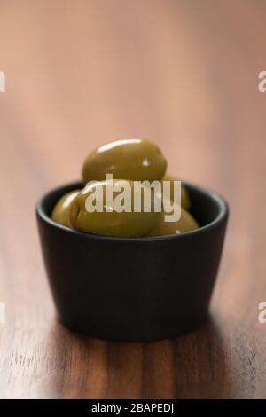 Riesige grüne Oliven in schwarzer Schale auf Walnusstisch Stockfoto