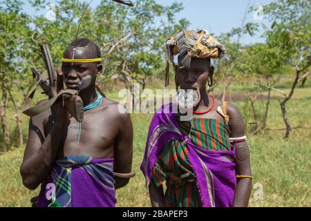 Ein Mann und eine Frau aus dem Mursi-Clan der Mann, der Kalaschnikow-Gewehr hält Stockfoto