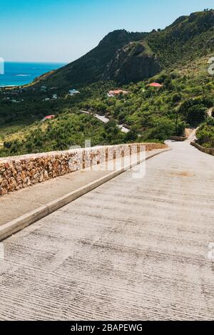 Eine malerische Straße hinunter zum Meer mit einer kleinen Steinmauer auf der Insel St. Barthélemy, französische Karibik Stockfoto