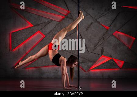Wunderschönes Mädchen, das akrobatische und flexible Tricks auf der Stange im Tanzstudio macht Stockfoto