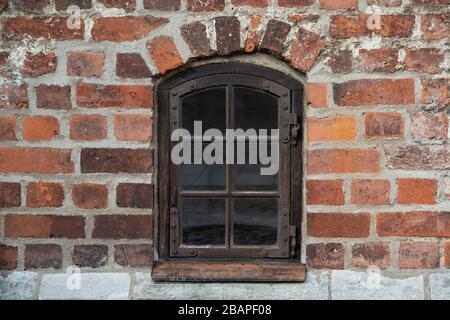 Antikes Holzfenster mit Metallbeschlägen und Scharnieren in einer alten roten Ziegelwand eines alten europäischen Schlosses. Stockfoto