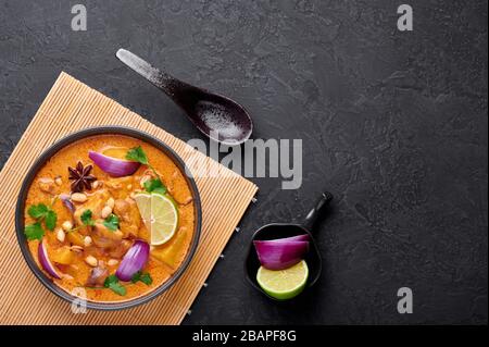 Ein Huhn Massaman Curry in schwarzer Schüssel mit dunklem Schieferhintergrund. Massaman Curry ist ein thailändisches Gericht mit Hühnerfleisch, Kartoffel, Zwiebel und vielen Gewürzen. Stockfoto