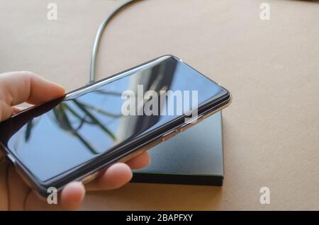 Weibliche Hand bringt das Telefon zum kabellosen Ladegerät. Kabelloses Ladegerät Stockfoto