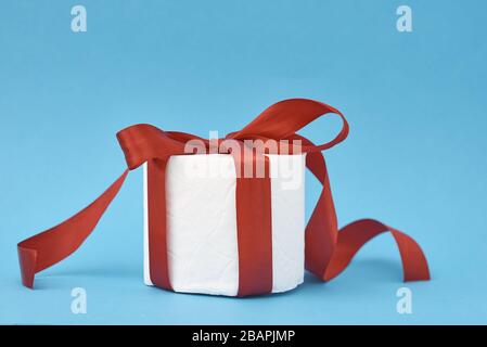 toilettenpapier in festlich-rotem Band als Geschenk auf blauem Hintergrund verpackt Stockfoto