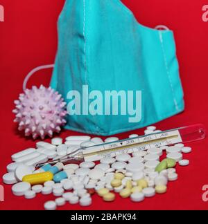 Schutzmaske, Medikamente und Thermometer auf rotem Hintergrund. Stockfoto