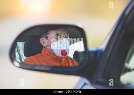 Ein Mann mit medizinischer Gesichtsmaske und Schutzbrille während einer Epidemie im Auto Stockfoto